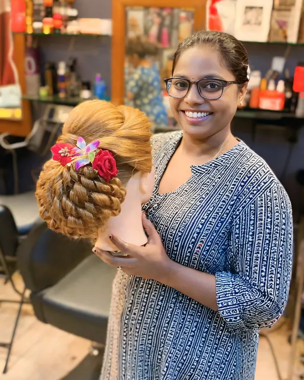 A happy student proudly displaying her finished bridal updo. She has masterfully created a twisted bun with floral accessories, ready for a real bride.