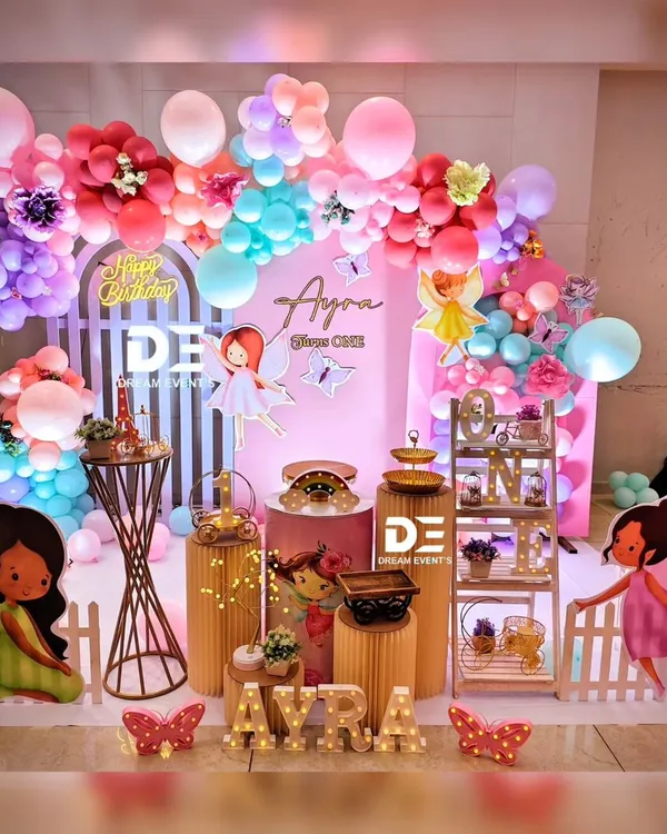 A fairy-themed first birthday party, complete with colorful fairy cutouts, a vibrant balloon arch, and custom light-up letters spelling the birthday girl's name.