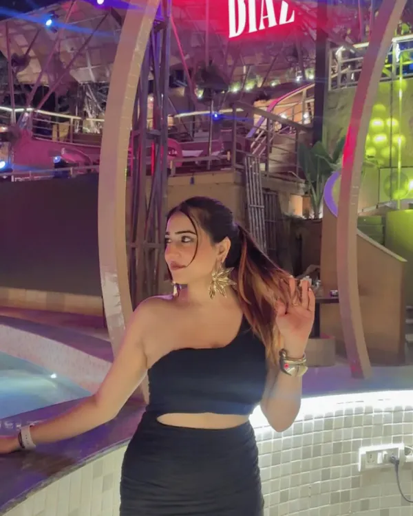 A sleek, one-shoulder black dress for a night out. The poolside setting and neon lights create a perfect party atmosphere.