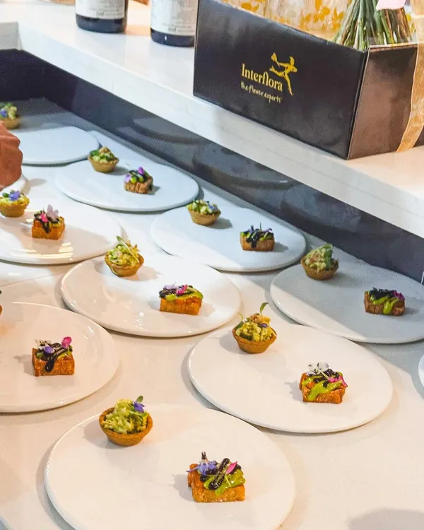 A wide shot of canapés being plated for a private event, in partnership with Interflora for the beautiful floral arrangements.