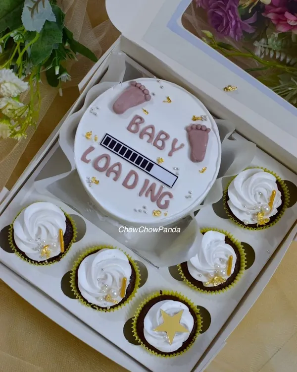 This bento cake and cupcake set was for a special baby shower. The design features a 'Baby Loading' theme on a mini choco-vanilla cake, surrounded by six matching cupcakes with simple white frosting and gold star details.