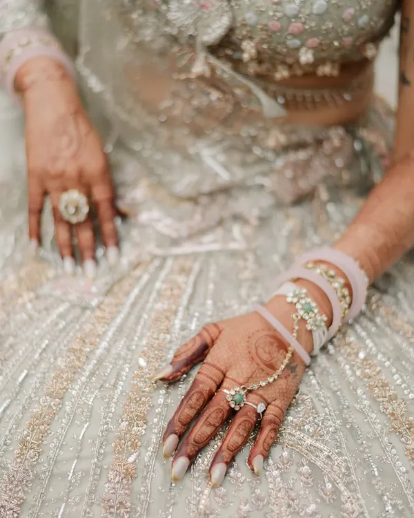 A close-up on the bride's hands, showcasing the intricate henna, the delicate hand jewelry, and the texture of her stunning lehenga. These details tell a story of tradition and personal style.
