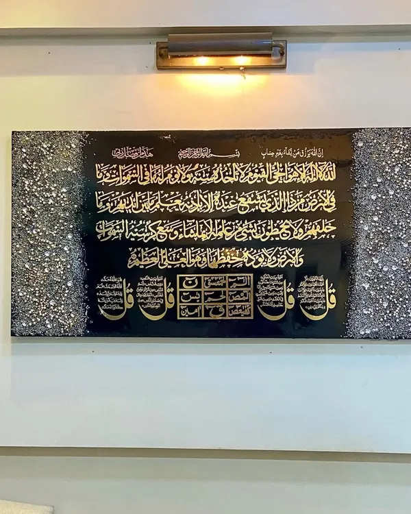 A client's wall featuring a comprehensive art piece. It includes Ayat al-Kursi, the Four Quls, and the Loh e Qurani, all rendered in striking gold calligraphy on a black resin background, framed by textured crystal borders.