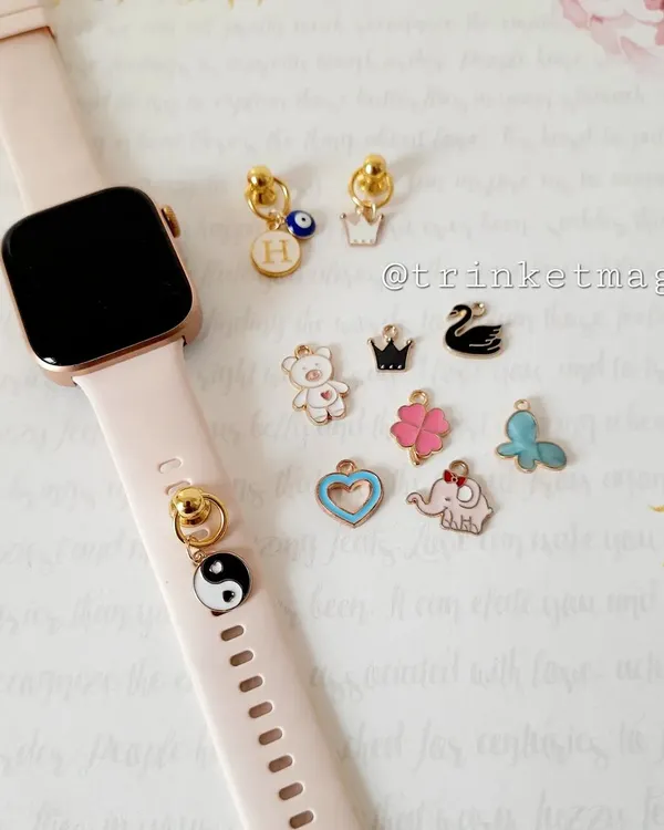 Make your smartwatch even smarter with these cute charms. This image shows a collection of enamel charms like a yin-yang, crown, evil eye, and teddy bear that can be attached to your watch band.