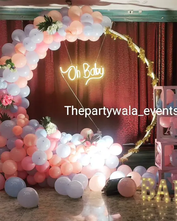 A beautiful "Oh Baby" baby shower setup with a cascade of pastel pink and blue balloons. The neon sign and "BABY" light-up letters create a perfect photo spot for the parents-to-be.