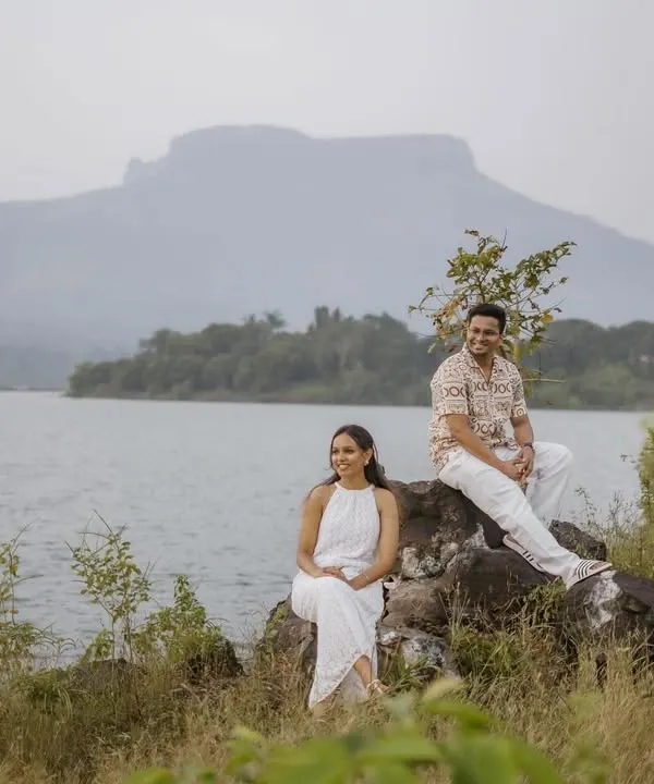 A stunning wide-angle shot of a couple seated by a tranquil lake, with a majestic mountain in the background. This showcases the epic scale of a destination pre-wedding shoot.