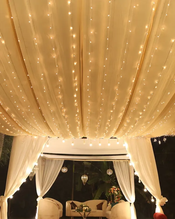 A romantic seating area under a canopy of draped fabric and warm fairy lights.