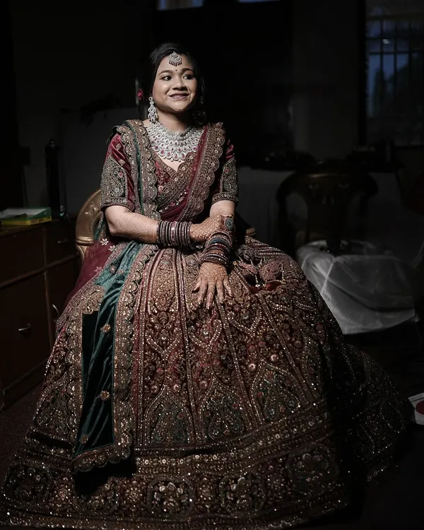A stunning full-length portrait of a North Indian bride in her magnificent, heavily embroidered lehenga. The low-light setting adds a touch of drama and elegance.