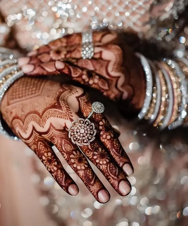 A close up of the bride's hands, showcasing her stunning rings and bracelets against the intricate mehndi. The sparkling details of her outfit create a beautiful, glittering backdrop.