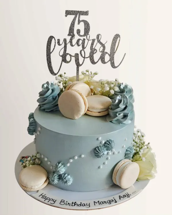 A beautiful and elegant cake to celebrate a 75th birthday. This design features a soft blue whipped cream finish, delicate silver details, and is adorned with fresh flowers and macarons.
