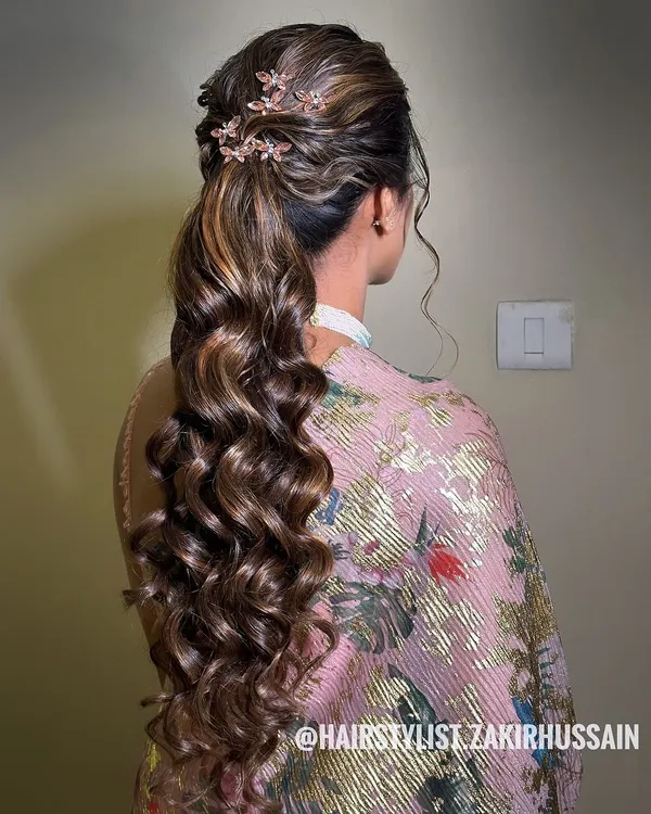 A glamorous ponytail with voluminous curls and a twisted crown, adorned with delicate floral clips. This style is perfect for adding a touch of elegance to a modern outfit.