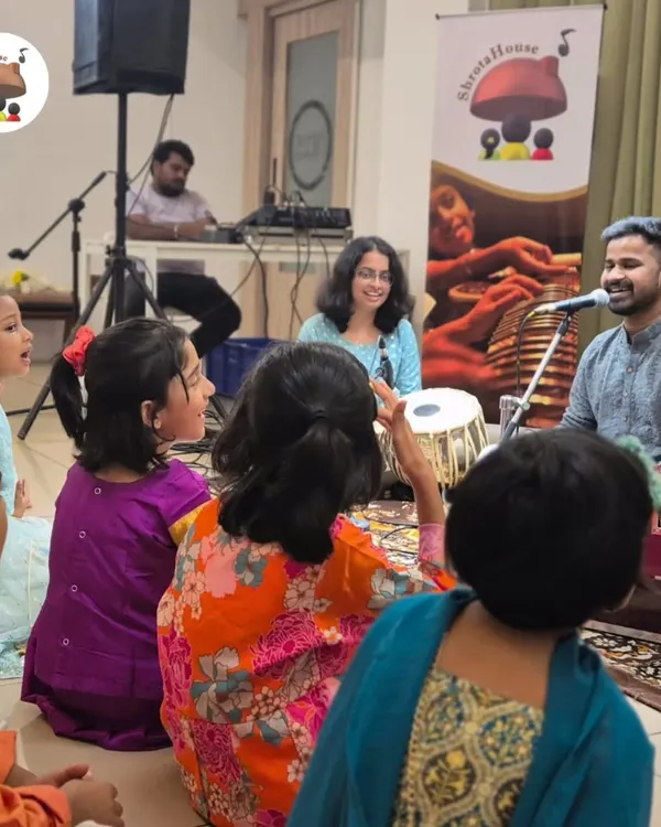An interactive session in full swing. Our students gather around to learn from a visiting artist, absorbing the rhythms of the harmonium and tabla in a fun, group setting.
