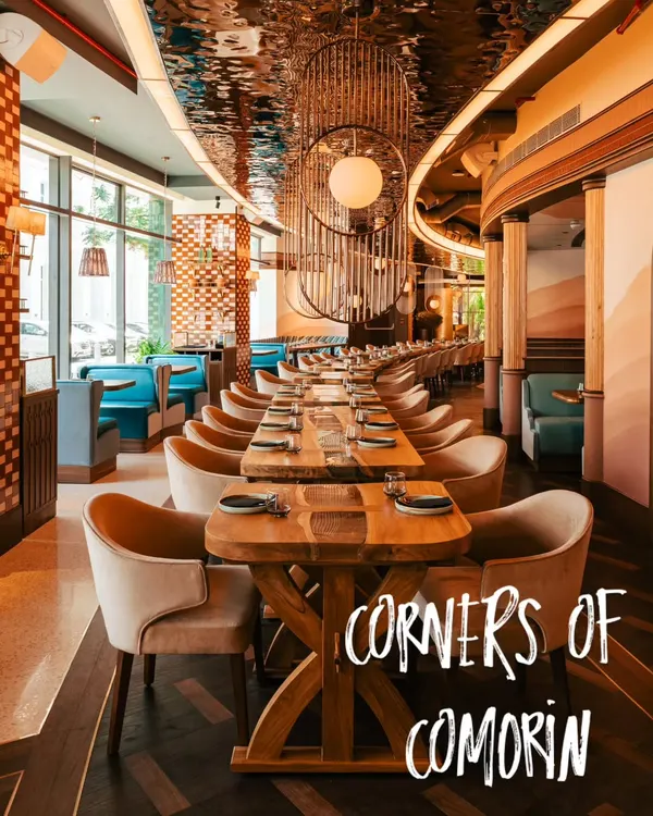 An expansive shot showcasing the stunning interior of Comorin. We captured the long dining table, unique light fixtures, and reflective ceiling to convey the restaurant's sophisticated design and grand scale.