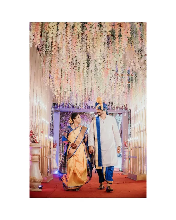 The grand walk as husband and wife. The couple walks hand in hand under a beautiful floral canopy, a perfect moment captured from their Maharashtrian wedding ceremony.