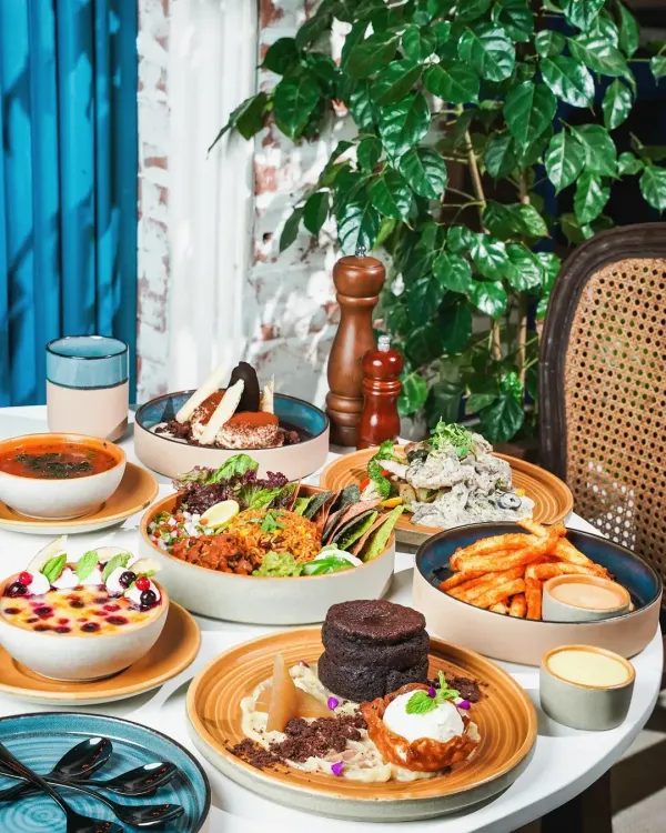 A full brunch spread at a bright and airy cafe, featuring a variety of dishes from salads and bowls to decadent desserts. This shot captures the lively, bustling atmosphere of a popular brunch spot.