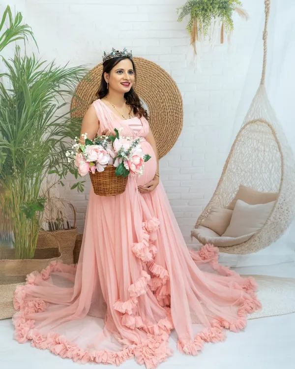 A beautiful princess-style portrait in our boho studio setup. The mom-to-be looks radiant in a pink gown and tiara, holding a basket of flowers.