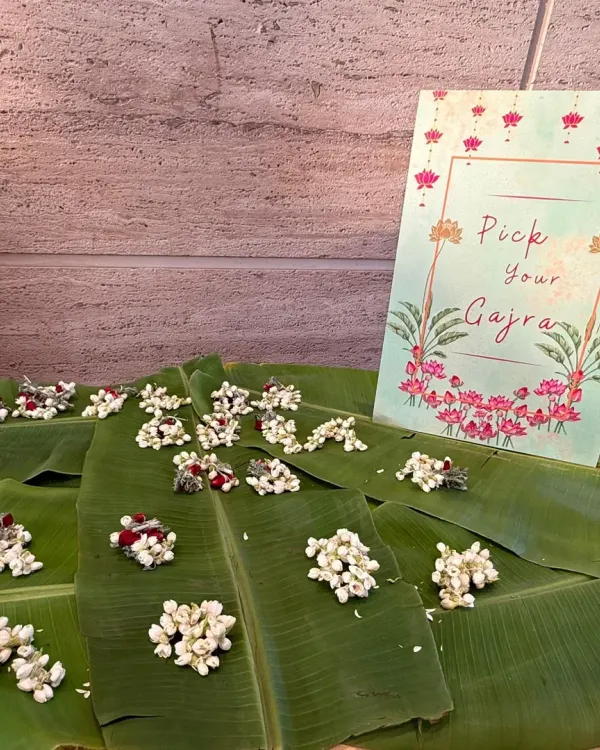 A charming "Pick Your Gajra" station is a wonderful traditional touch for any Indian celebration. Here, fresh jasmine gajras are beautifully displayed on banana leaves with a custom-designed sign, inviting guests to adorn themselves with fragrant flowers.
