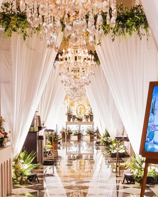 A breathtaking entrance gallery for a Mehendi, with a reflective floor, cascading chandeliers, and lush greenery. I design these immersive pathways to wow your guests from the moment they arrive.