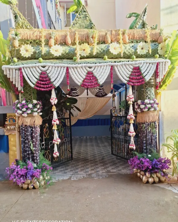 A full front view of an elaborate and traditional entrance decoration, perfect for a housewarming. The design uses sugarcane, banana leaves, coconut shells, and extensive floral work to create a grand and auspicious welcome.