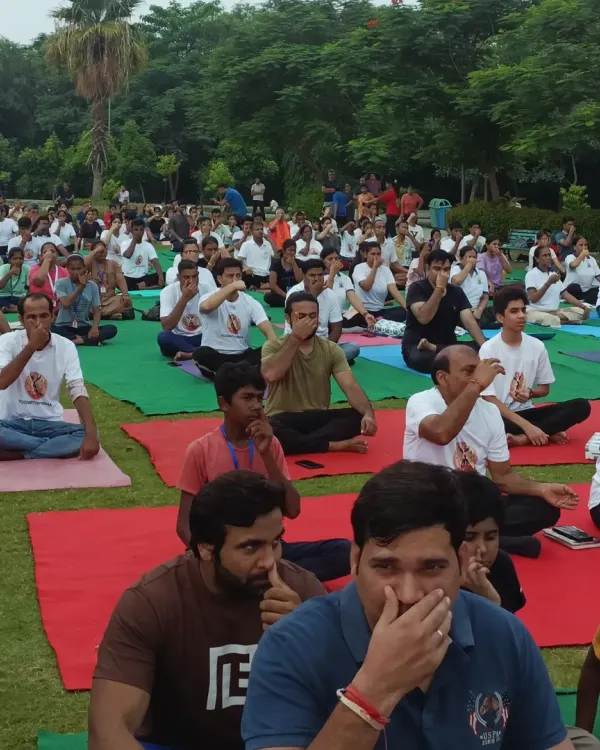 A large group practicing pranayama together in a lush green park. There is a special energy when a community comes together to practice in nature.