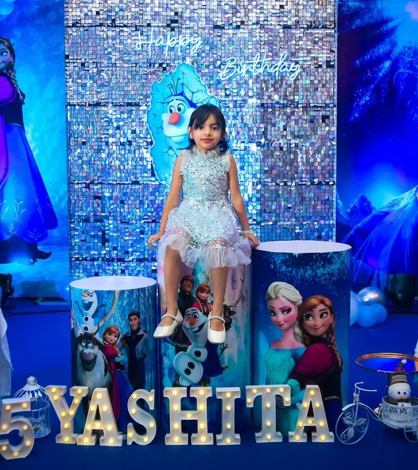 A spectacular Disney Frozen theme for a 5th birthday celebration. The entire venue was transformed into a winter wonderland with shades of blue and silver, a sequin backdrop, and life-sized cutouts of Elsa, Anna, and Olaf.