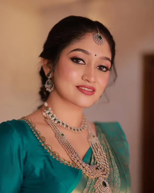 This is my signature radiant bridal look. I focused on creating flawless, glowing skin with a classic winged eyeliner and a bold red lip, which perfectly complements the client's beautiful teal and gold Kanjivaram saree.