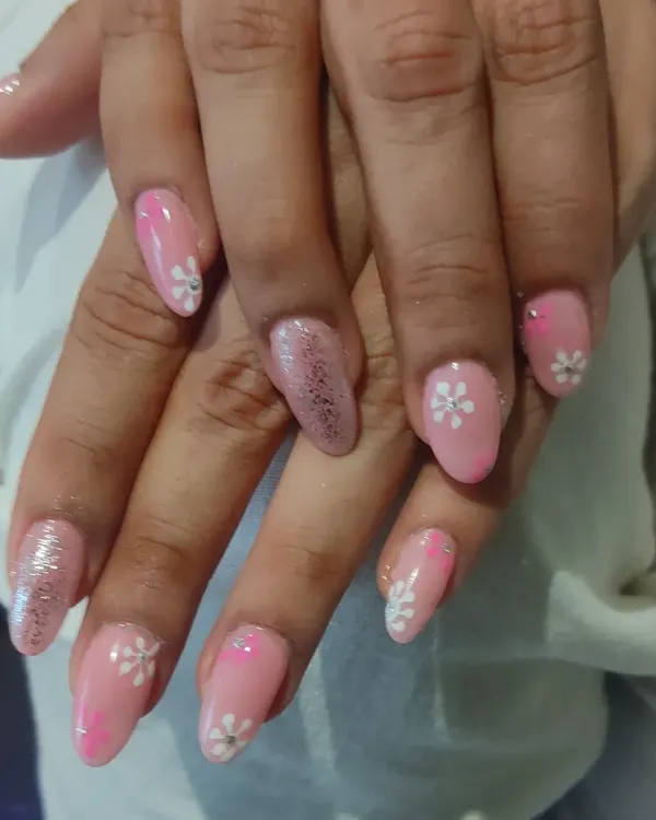 A sweet and feminine design featuring a soft pink base with hand-painted white daisy flowers and a single glitter accent nail.