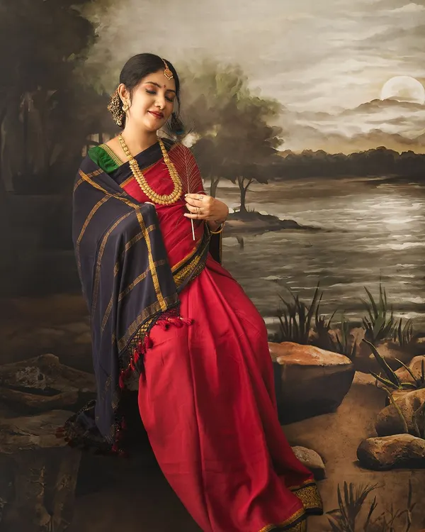 A stunning maternity portrait inspired by classical Indian art. The expectant mother sits by a painted river scene, holding a feather, creating a look of serene elegance.