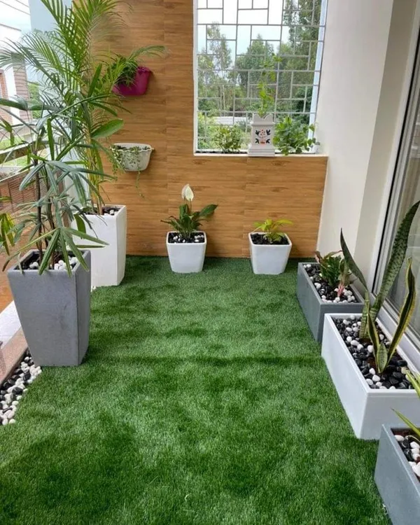 A modern balcony makeover featuring a lush artificial lawn bordered by decorative pebbles. We used sleek, minimalist planters and a wood-paneled accent wall to create a clean and contemporary green space.