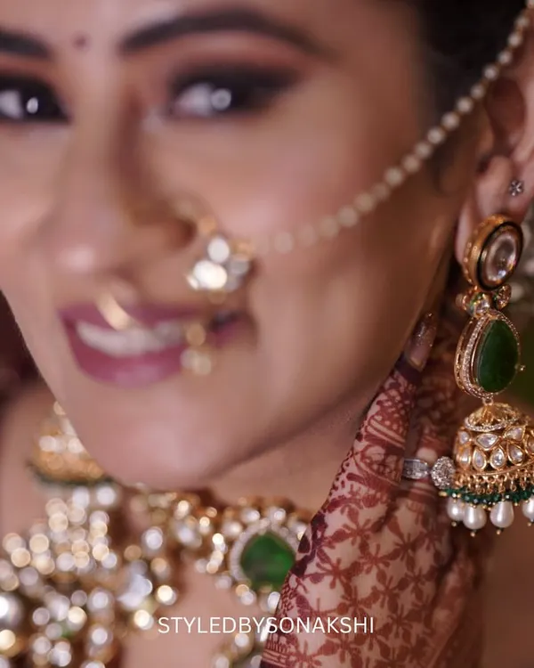 A close-up on the exquisite details of a bridal look. This shot highlights the beautiful kundan and emerald jhumkas and the delicate nath, which add a touch of tradition and color to the bride's ensemble.