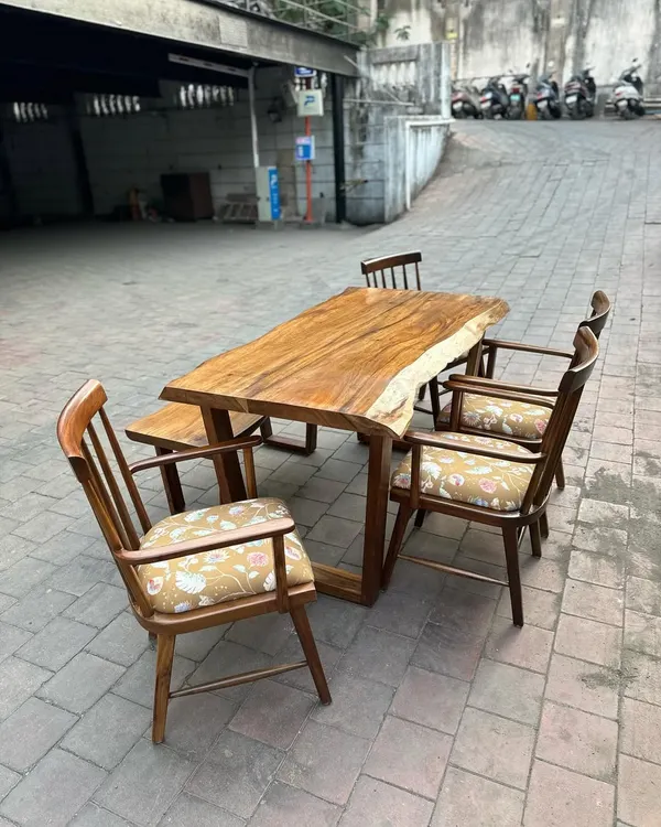 A live-edge dining table made from a single slab of wood, paired with classic chairs and a matching bench. The natural edge of the wood makes each table a unique piece of art.