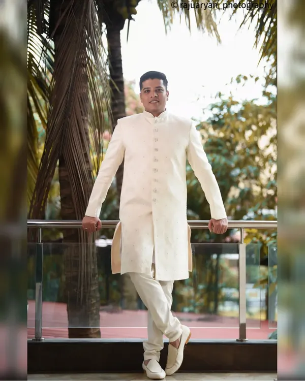 A stylish, full-length portrait of the groom in his elegant off-white sherwani. His relaxed yet confident pose on the balcony makes for a great shot.