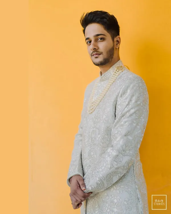 A stylish portrait of the groom against a vibrant yellow wall. His elegant sherwani and confident pose make for a striking and modern groom portrait.