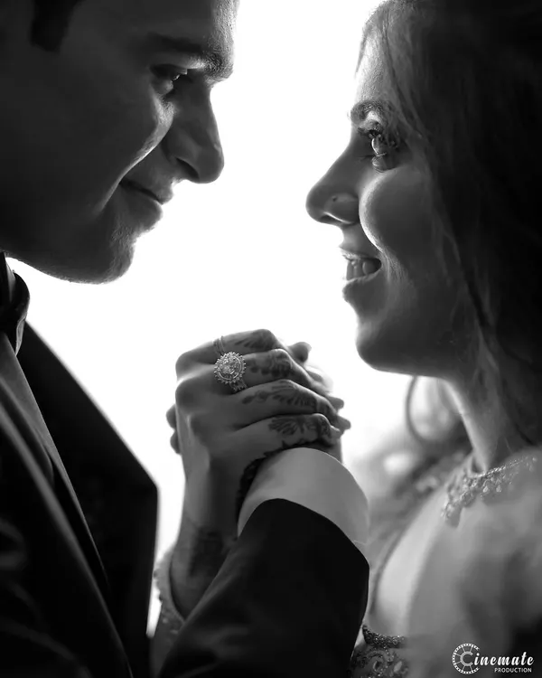 A powerful black and white close-up focusing on the couple's hands and expressions. The high contrast and backlighting create a dramatic and intimate portrait, highlighting the engagement ring and their connection.