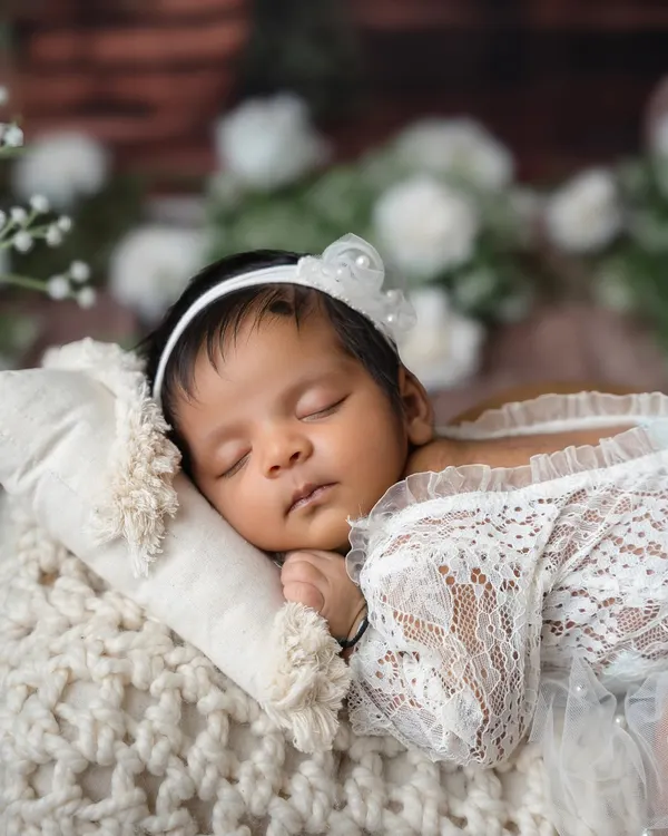 A close-up of a sleeping newborn, dressed in delicate white lace and a pearl headband. I focus on capturing their angelic features and peaceful expressions.