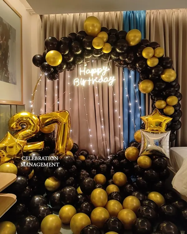 A classic and bold choice for a 27th birthday. This circular balloon arch in black and gold is paired with a 'Happy Birthday' neon sign for a sophisticated party look.