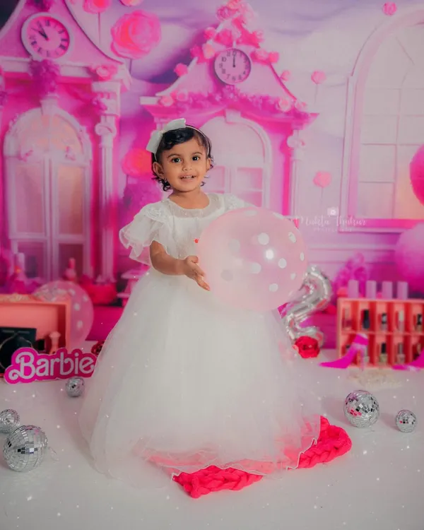 Our two-year-old Barbie princess holding a balloon, looking absolutely radiant in her beautiful white gown against the pink dollhouse backdrop.