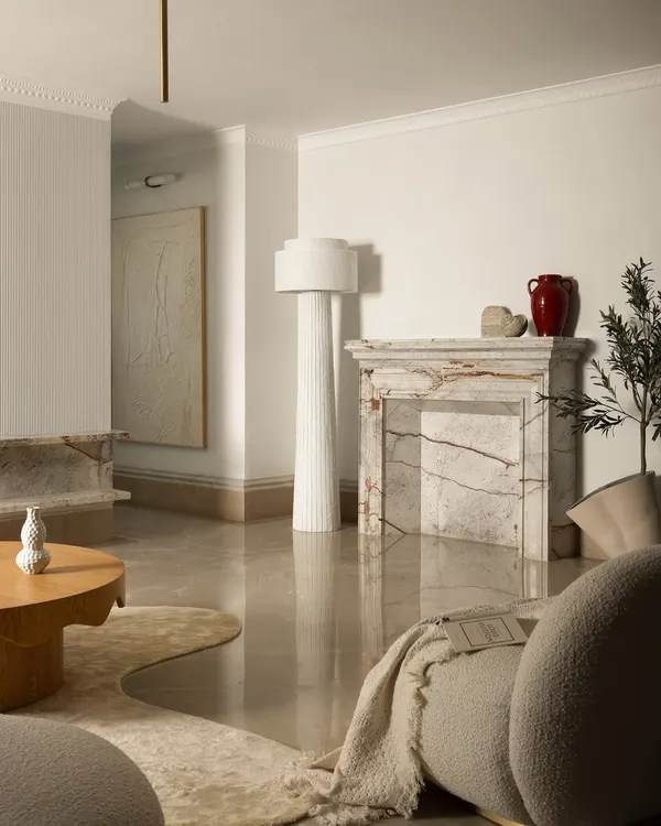 A view of the Ecru Maison living room, where a sculptural marble fireplace and a fluted floor lamp add layers of texture. We focused on a mix of organic forms and natural materials like oak and boucle to create a space that feels both modern and timeless.