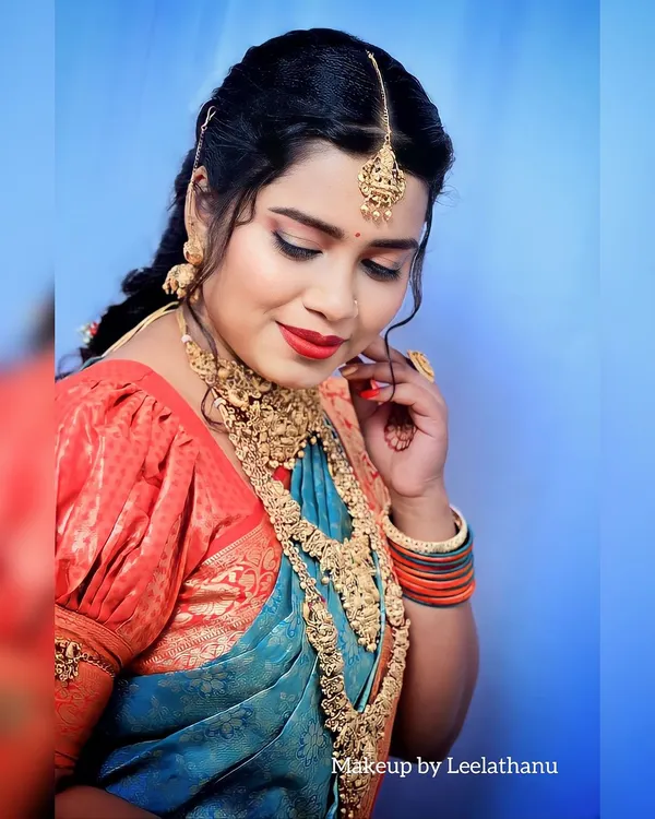 A stunning bridal photoshoot look. This features dramatic eye makeup, a bold red lip, and elaborate temple jewelry, showcasing a high-fashion bridal style.