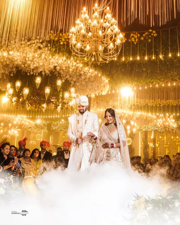A breathtaking entry for a fairytale wedding. The couple walks through a cloud of smoke under a grand chandelier, a perfect example of the cinematic and grand wedding moments I love to capture.