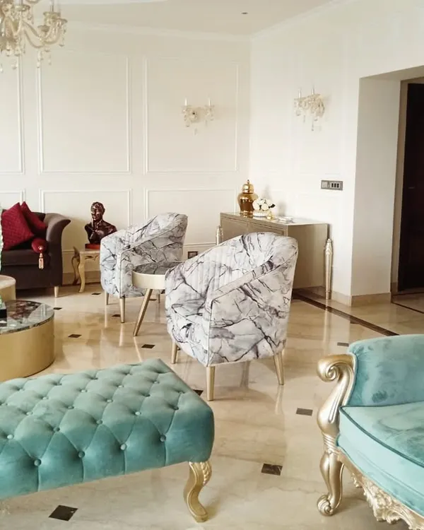 A complete view of a luxurious living room we designed, featuring a mix of custom furniture. This includes a classic brown sofa, a tufted turquoise bench, a matching armchair with ornate gold-finished legs, and modern patterned accent chairs, all arranged on a polished marble floor.