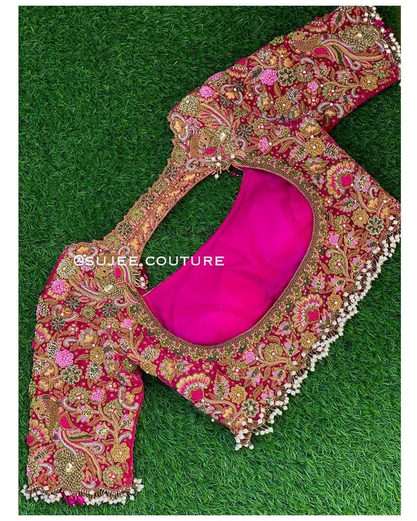 A classic velvet bridal blouse in a rich pink hue. This piece is designed for a gold Kanchipuram saree and features intricate zardozi and knot work, with pearl tassels along the waistline for added elegance.