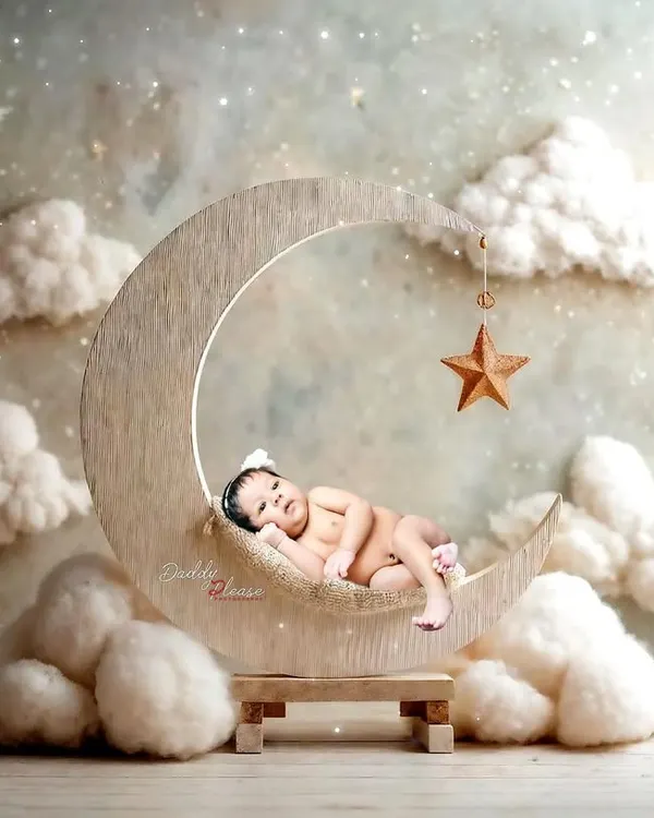 A peaceful newborn portrait featuring a baby sleeping on a wooden crescent moon prop, surrounded by soft, dreamy clouds. These sessions are designed to be calm and safe for your little one.
