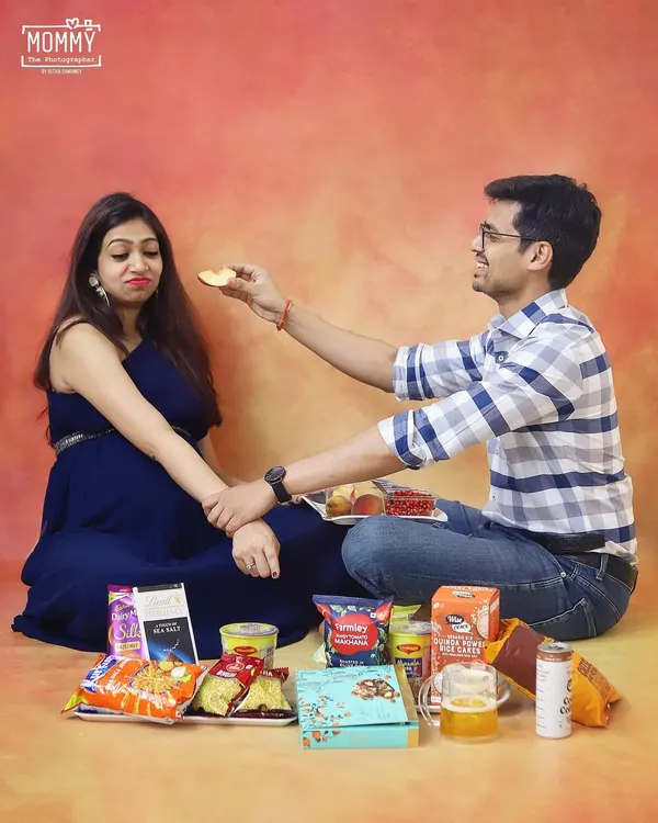 A funny and relatable take on pregnancy cravings. This playful studio shot captures the couple surrounded by snacks, adding a touch of humor to their maternity photoshoot.