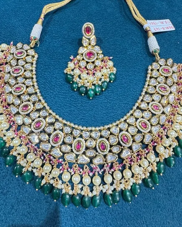 This beautiful kundan necklace set is a perfect example of fine making. It features high-quality kundan stones accented with ruby-red centerpieces and finished with elegant green beads and pearls.