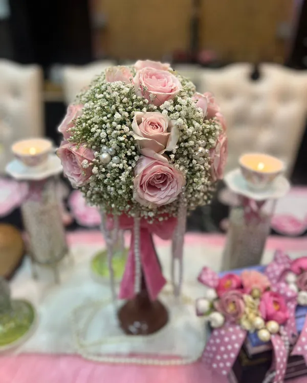 This is a centerpiece I created for a coquette-inspired theme. A lush bouquet of pink roses and baby's breath is accented with cascading pearls and a pink ribbon, creating a look of vintage romance and playful elegance.