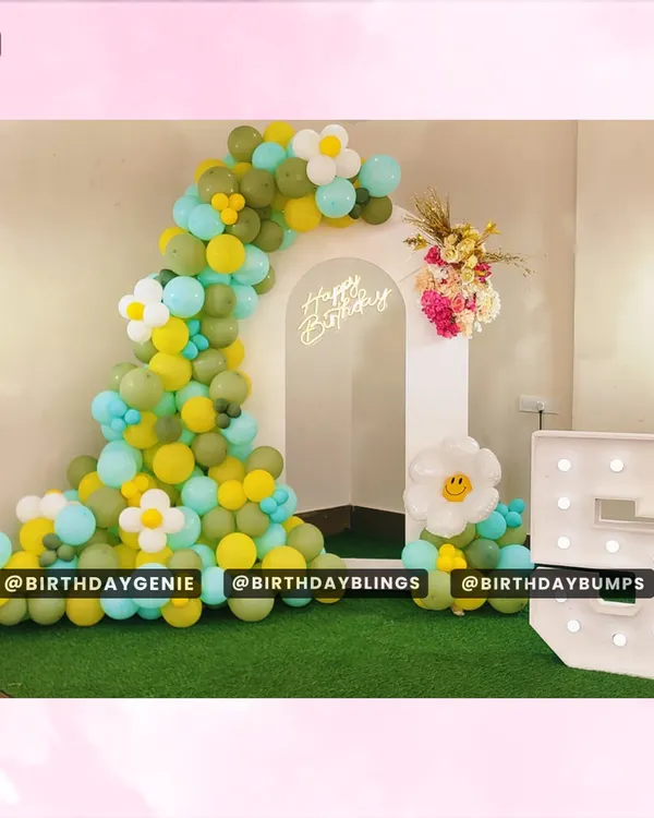 A cheerful and simple birthday setup with a daisy-flower balloon arch in green and yellow, a neon sign, and a light-up number '5'.