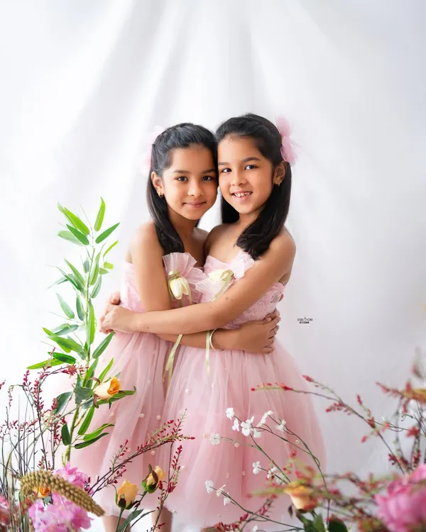 Two of a kind. These twin sisters share a sweet hug in their beautiful pink dresses, surrounded by a lovely floral setup for their 7th birthday photoshoot.