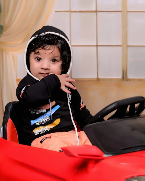 A close-up of our little driver, looking cool and confident in his ride. The black hoodie adds a stylish touch to this 6-month-old's car-themed photoshoot.