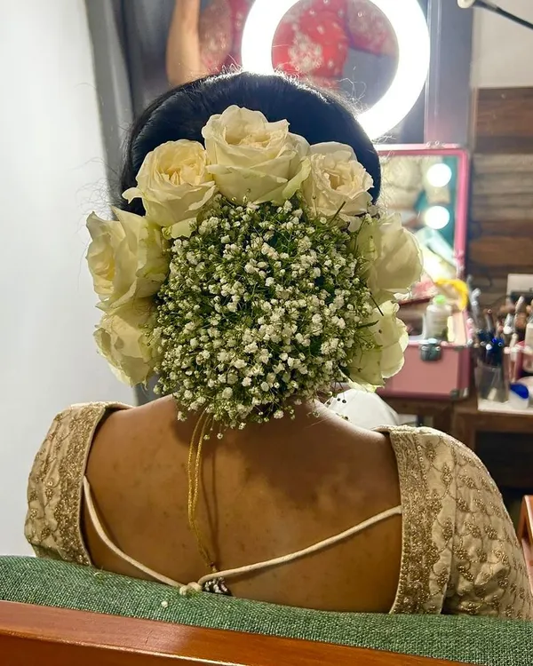 A stunning bridal bun adorned with a beautiful arrangement of fresh white roses and baby's breath. This is a classic and romantic choice for any bride.